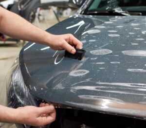 Person smoothing out plastic sheet on car hood
